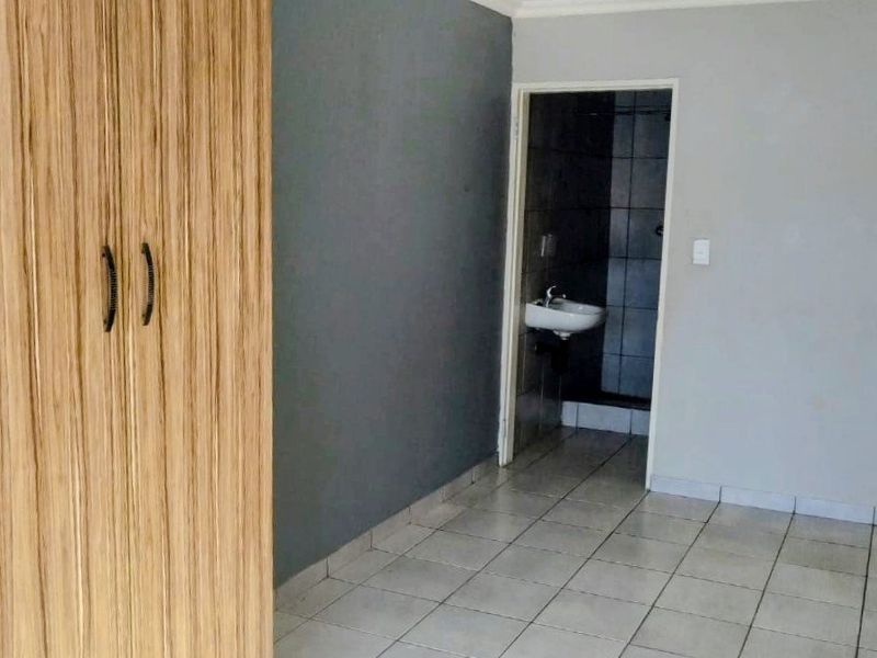 A clean, empty bedroom featuring tiled flooring, a built-in wooden wardrobe, and direct access to an en-suite bathroom.