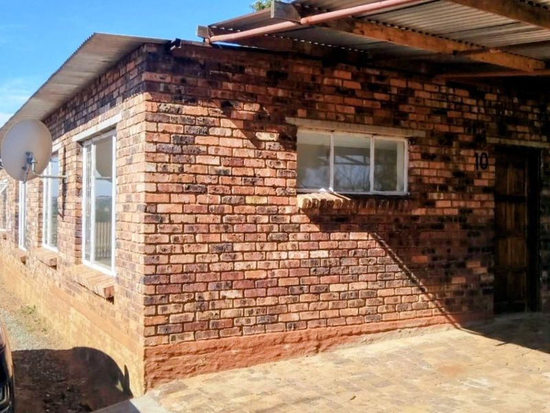 Front exterior view of a face brick apartment unit featuring a corrugated metal roof and paved driveway area.