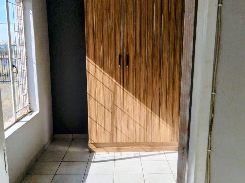 A compact bedroom featuring tiled flooring, a built-in wooden wardrobe, and natural light through a window with security bars.