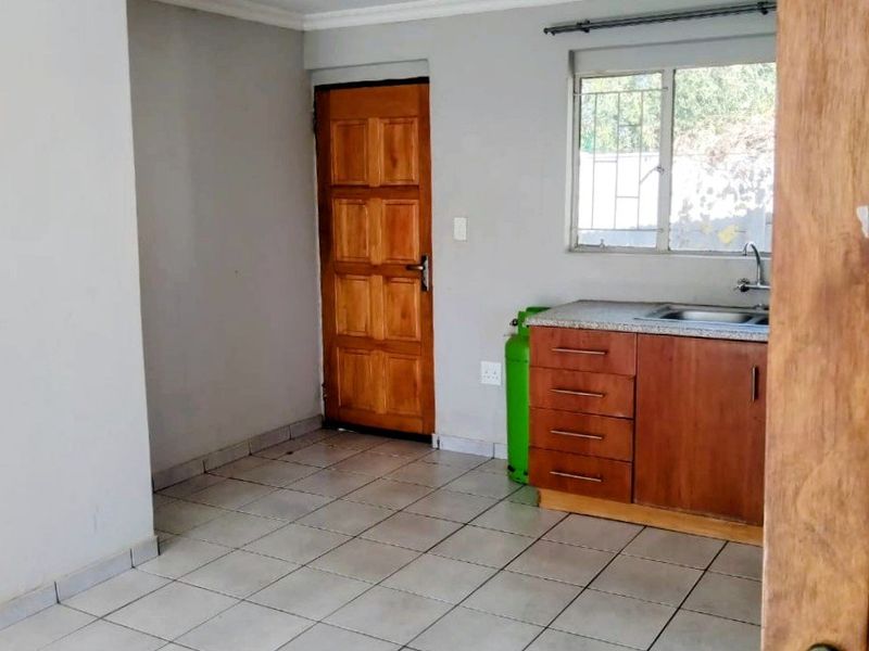 A compact, empty kitchen featuring tiled flooring, wooden cabinetry with a granite countertop, and a single sink, providing a functional base for renovation.
