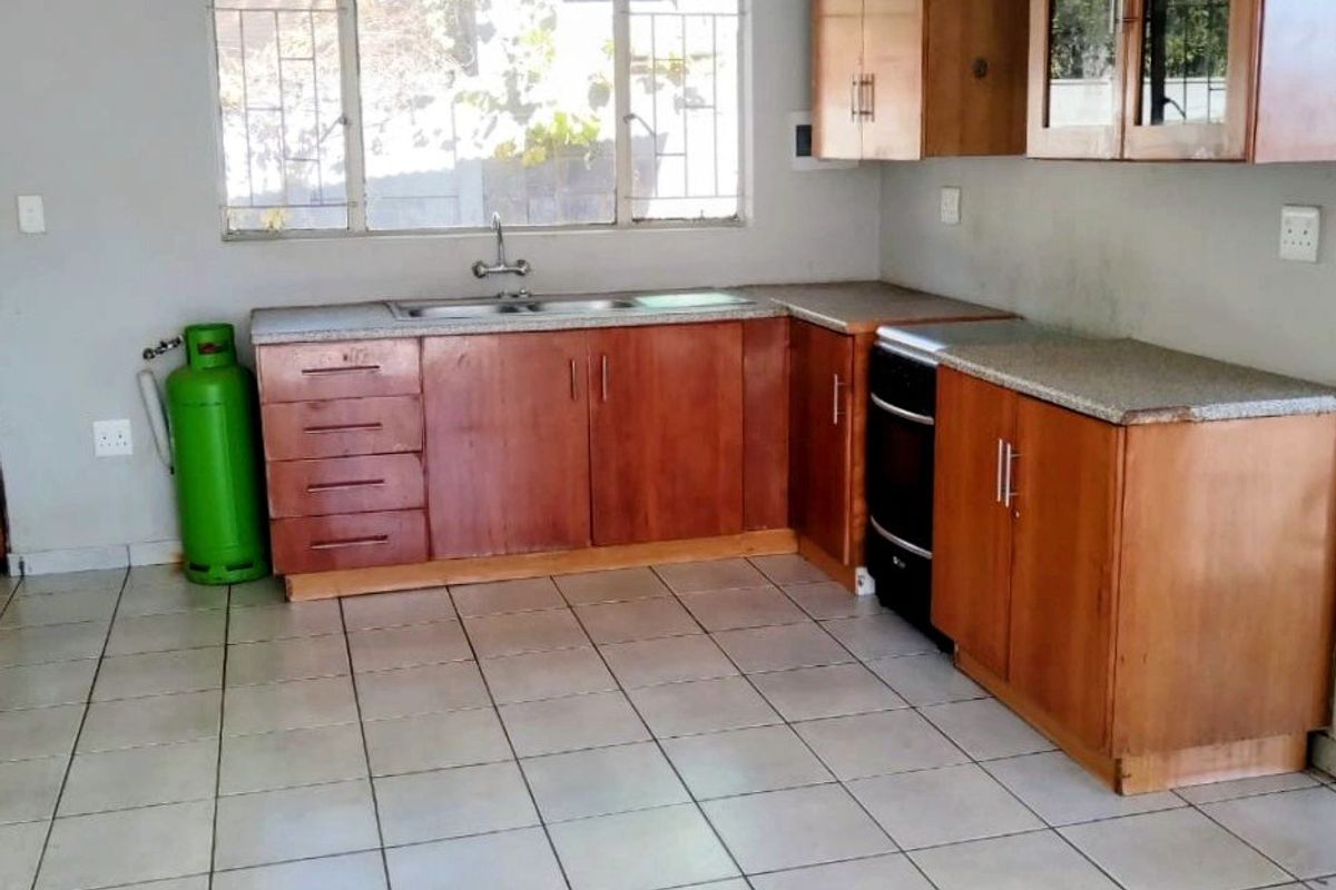 A functional kitchen featuring wooden cabinetry, stone countertops, a stainless steel sink, and ceramic tiled flooring, offering a clean and practical layout.
