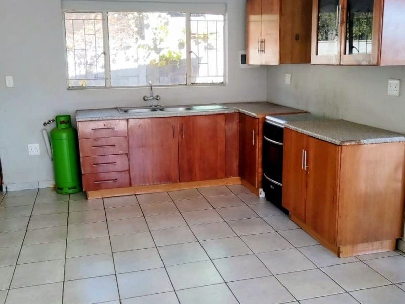 A functional kitchen featuring wooden cabinetry, stone countertops, a stainless steel sink, and ceramic tiled flooring, offering a clean and practical layout.