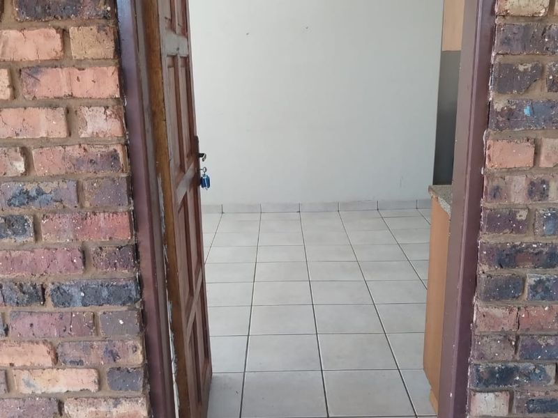 View through an open timber door into an empty interior space featuring tiled flooring and exposed brick exterior detailing.