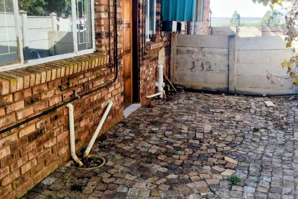 Rear exterior view of the apartment featuring exposed brick walls, cobblestone paving, and a precast concrete boundary wall.