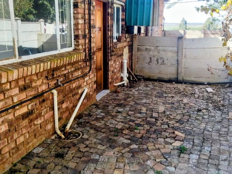 Rear exterior view of the apartment featuring exposed brick walls, cobblestone paving, and a precast concrete boundary wall.