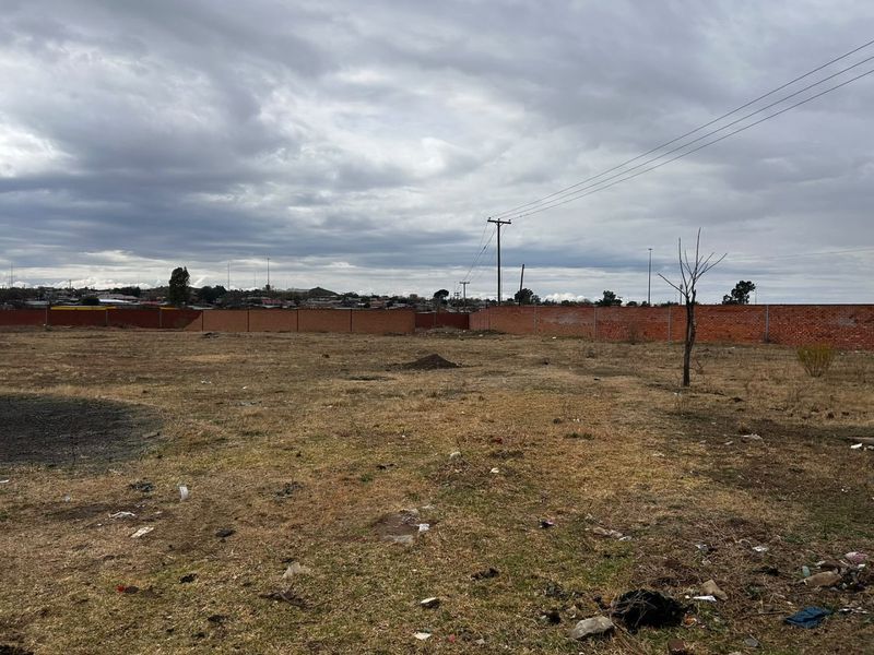 A large, vacant plot of land enclosed by a brick perimeter wall, featuring open ground and a utility pole.