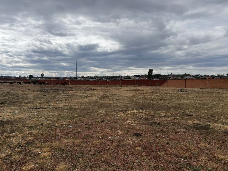 A large, undeveloped plot of land featuring a brick boundary wall and open field space.