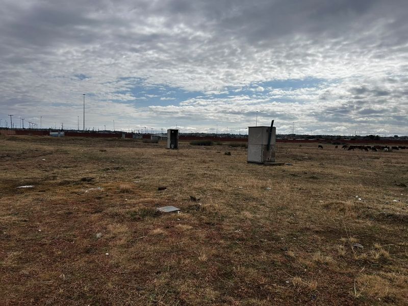 An expansive, undeveloped plot of land featuring sparse vegetation and distant perimeter fencing under a cloudy sky.