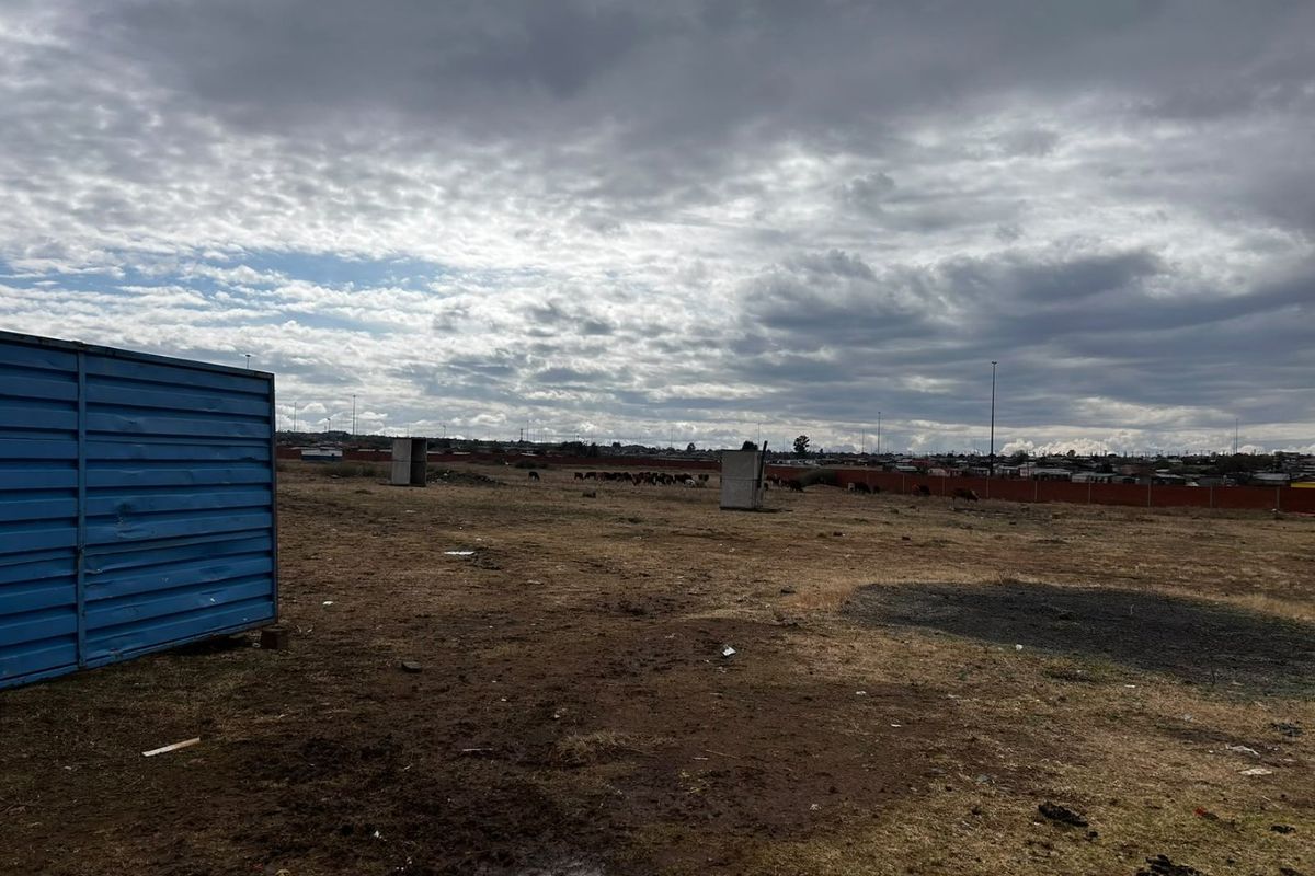 A large, undeveloped plot of land featuring perimeter fencing and open terrain under a cloudy sky.