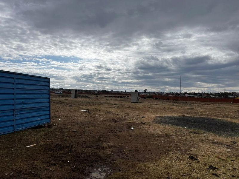 A large, undeveloped plot of land featuring perimeter fencing and open terrain under a cloudy sky.