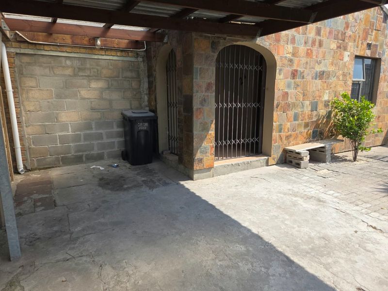 Exterior view of a home entrance featuring stone cladding, a concrete driveway, and a timber pergola structure over the entryway.