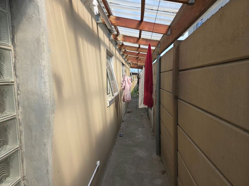 A narrow side utility passage featuring a concrete floor, precast boundary wall, and a translucent roof structure providing covered outdoor storage or service space.