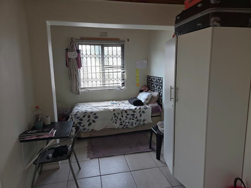 A functional bedroom featuring tiled flooring, a security gate on the window, and built-in storage space.