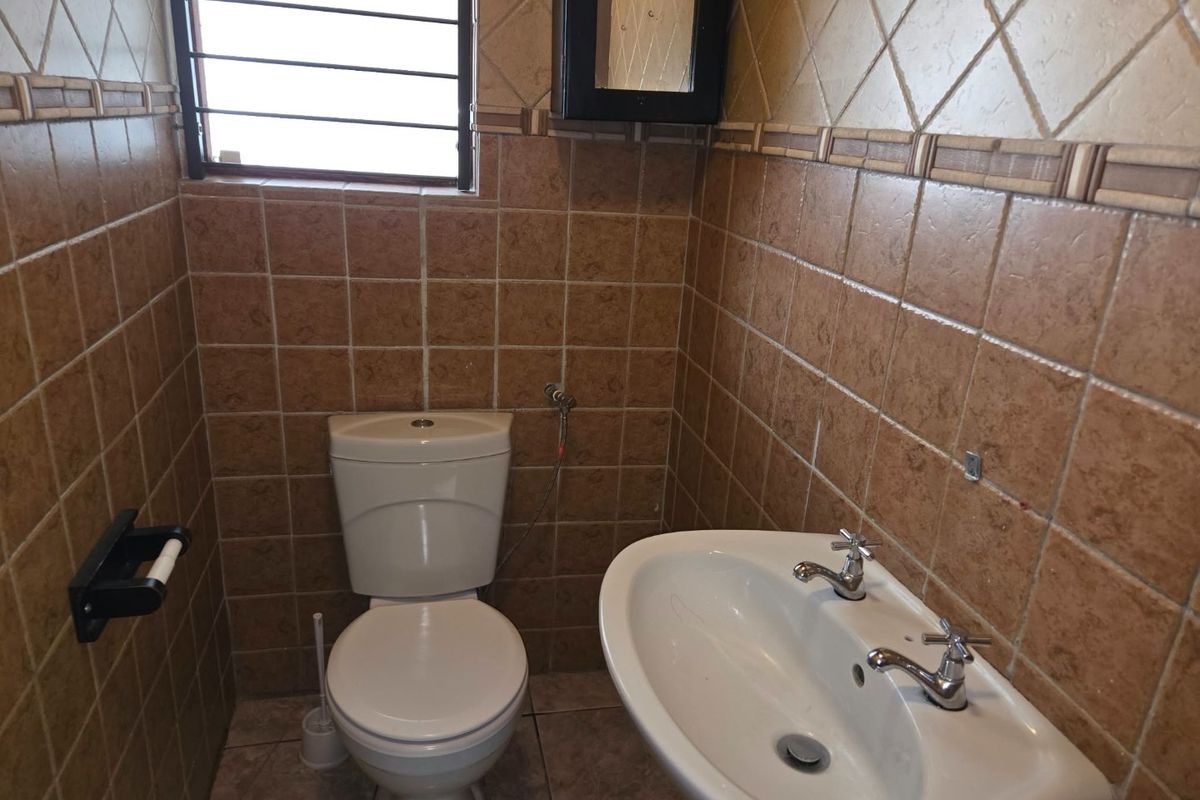 A compact bathroom featuring full-height ceramic wall tiling, a pedestal basin, and a standard dual-flush toilet.