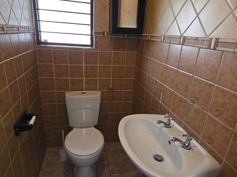 A compact bathroom featuring full-height ceramic wall tiling, a pedestal basin, and a standard dual-flush toilet.