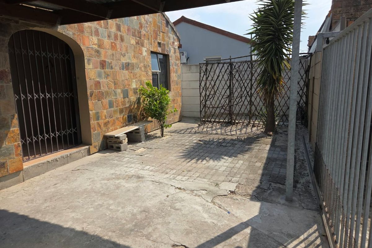A rear exterior patio area featuring stone cladding, concrete paving, and a covered section, offering a private outdoor space with potential for landscaping.