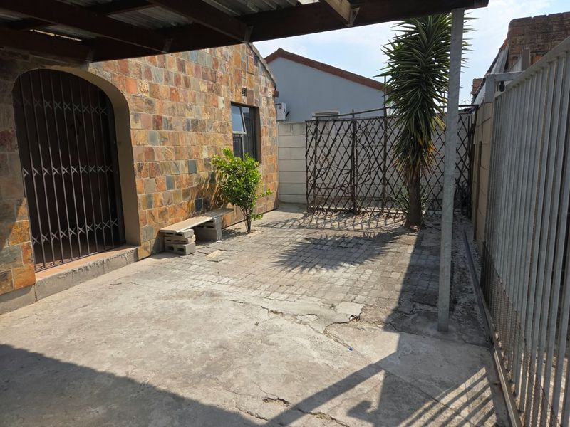 A rear exterior patio area featuring stone cladding, concrete paving, and a covered section, offering a private outdoor space with potential for landscaping.
