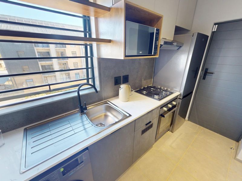 Modern kitchen featuring stone countertops, gas hob, built-in oven, extractor fan, and integrated microwave with sleek cabinetry and large window with security bars.