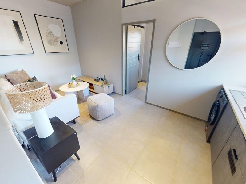 Modern open-plan living area featuring tiled flooring, integrated kitchen cabinetry with a built-in sink, and a washing machine, leading to an adjacent room.