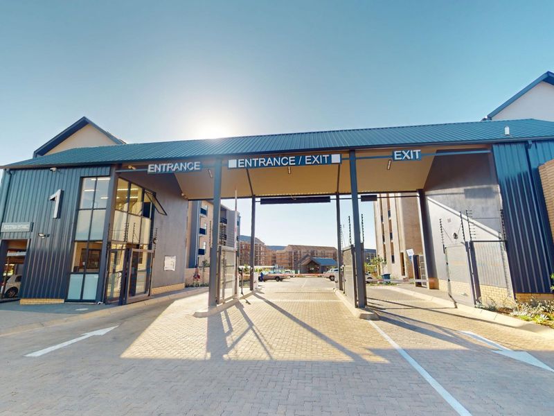 Secure gated entrance to the apartment complex featuring a paved driveway, metal roofing, and integrated security fencing.