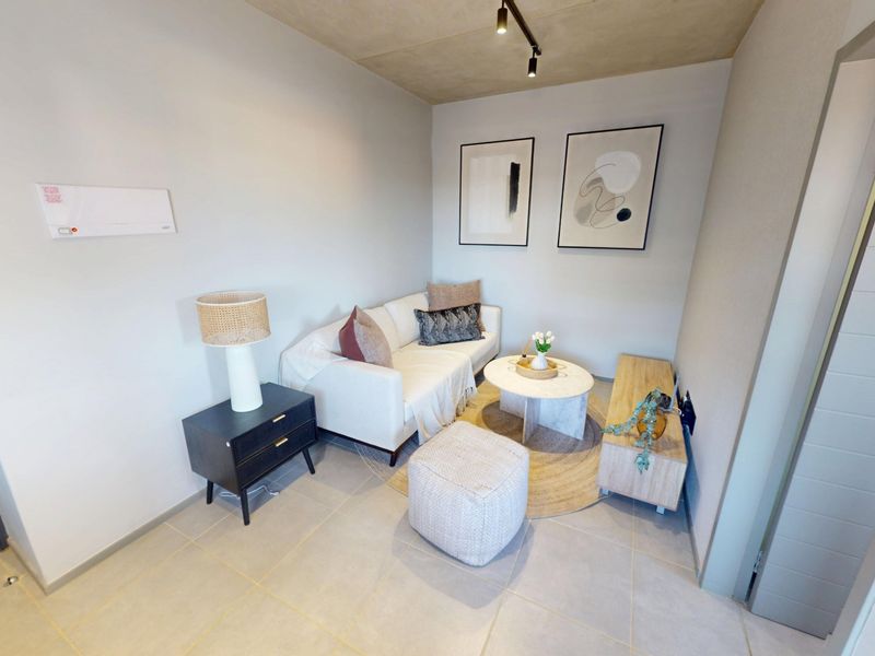 A compact living area featuring modern tiled flooring, an exposed concrete ceiling, and contemporary track lighting.