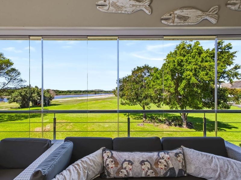 Enclosed balcony featuring glass stacker doors and a stainless steel balustrade, offering expansive views of the surrounding green landscape and river.