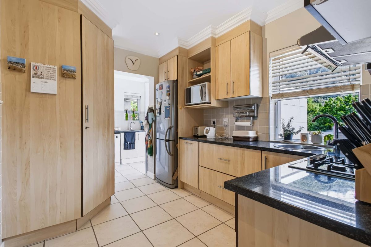 Functional kitchen featuring light wood cabinetry, granite countertops, built-in appliances, and tiled flooring, with an adjacent scullery area visible.
