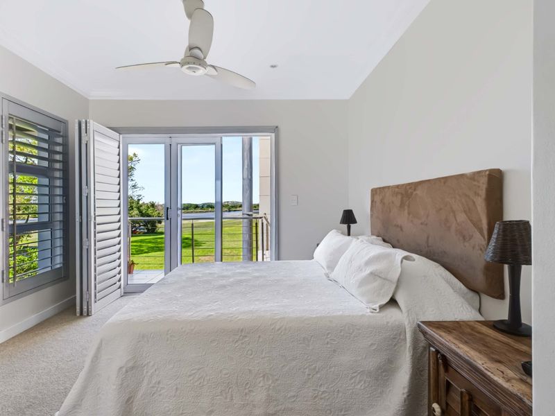 A bright bedroom featuring carpet flooring, a ceiling fan, and sliding glass doors that open onto a balcony with scenic views.