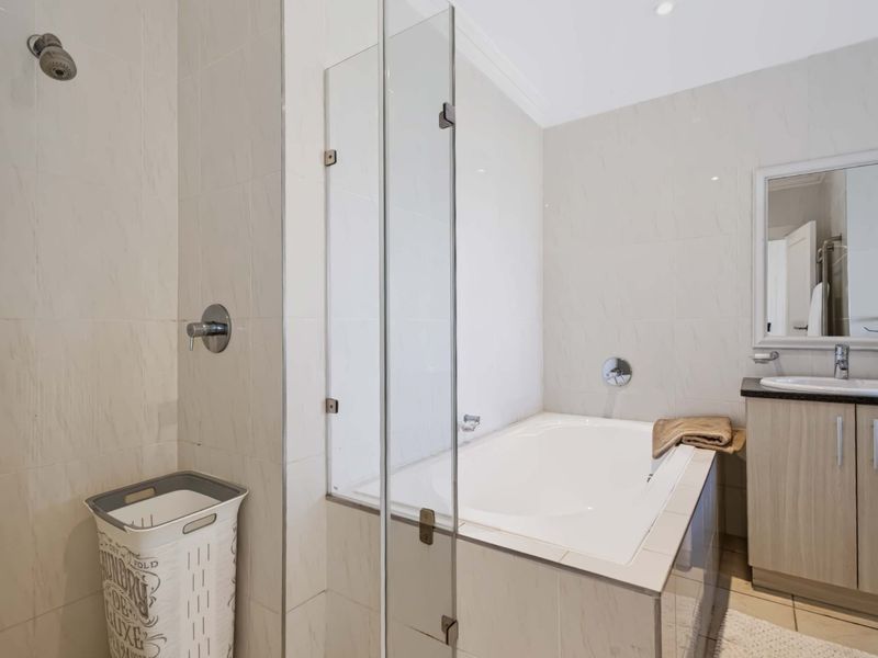 A clean, functional bathroom featuring a built-in bathtub with a glass screen, a separate shower area, and a vanity cabinet with an under-mount sink.
