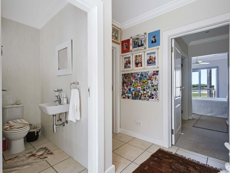 A clean, functional guest bathroom featuring a wall-mounted basin and toilet, with neutral tiled finishes and access to the adjacent living area.
