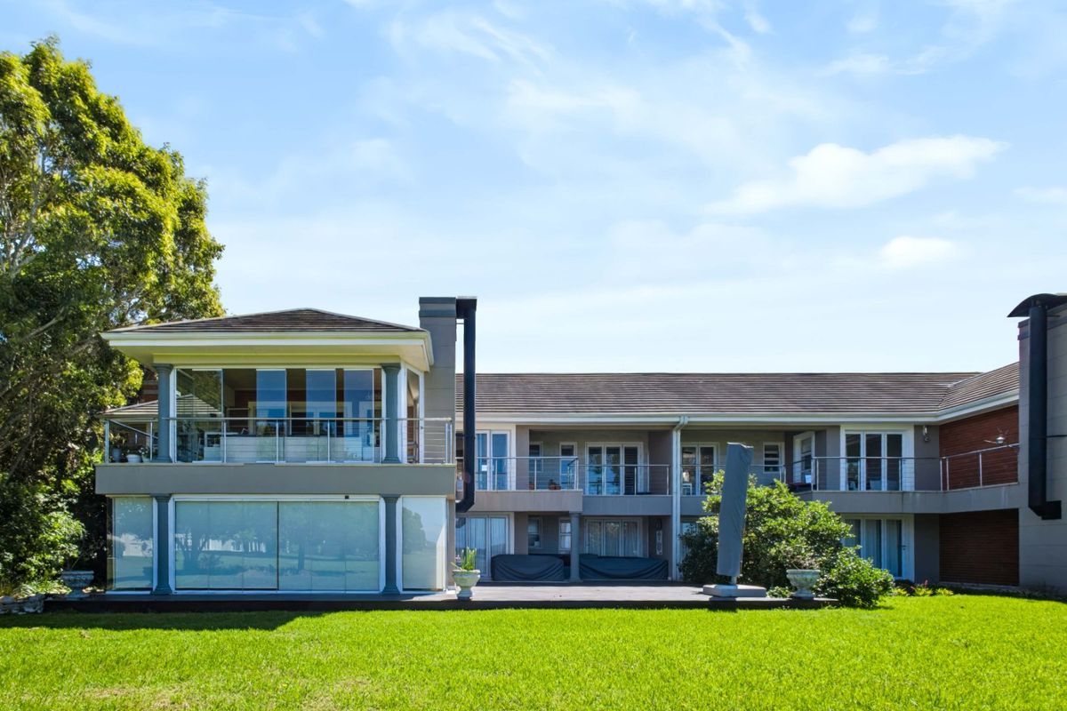 Rear view of the apartment building featuring a spacious lawn, wooden decking, multiple balconies with stainless steel railings, and large sliding glass doors.