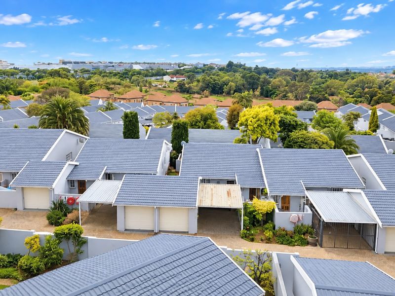 Aerial view of a townhouse complex featuring multiple units with tiled roofs, paved driveways, garages, and carports set within a landscaped residential estate.