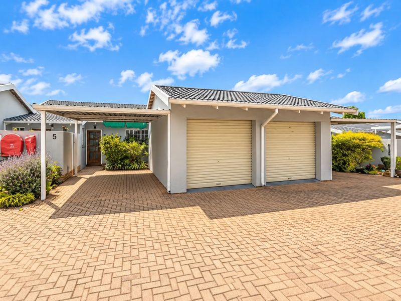 A well-maintained townhouse exterior featuring a double garage with roller doors and an additional covered carport area with paved driveway.