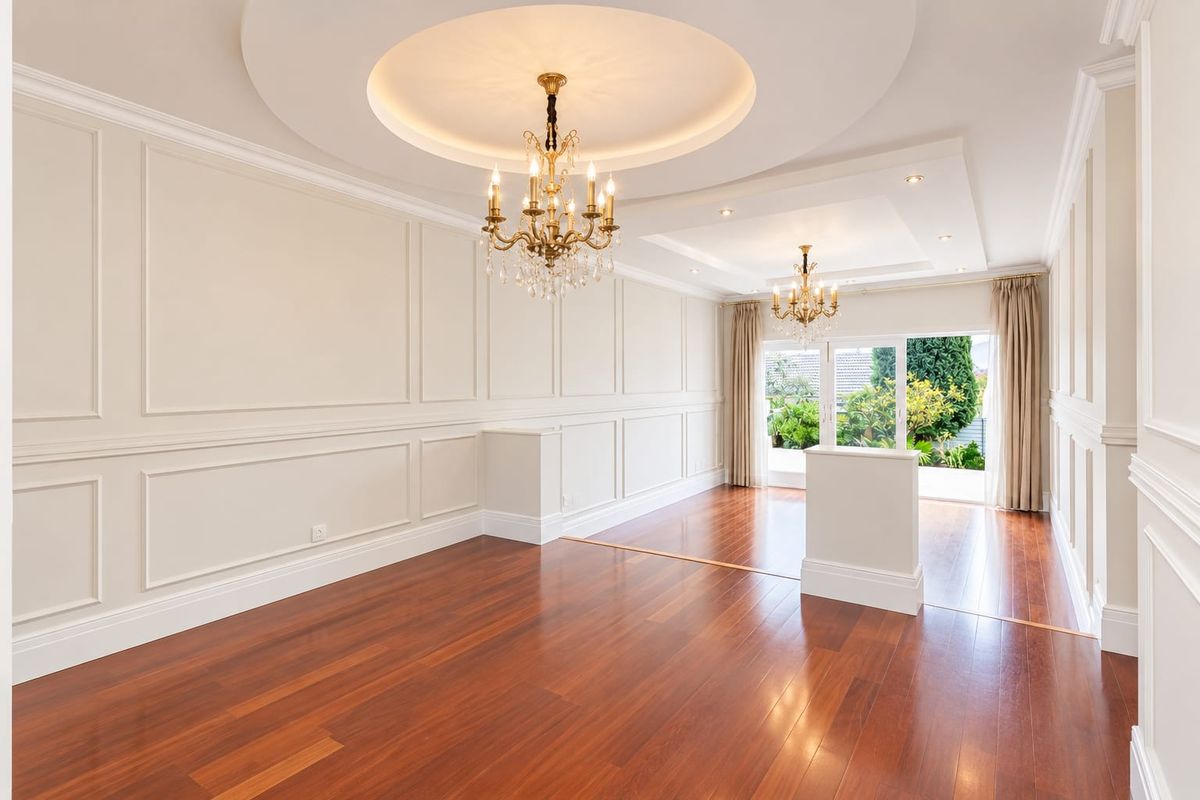 Spacious living area featuring elegant wainscoting, hardwood flooring, recessed ceilings with crystal chandeliers, and direct access to the garden through sliding glass doors.