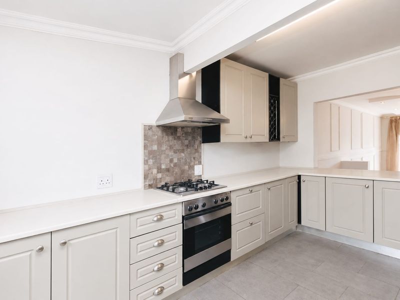 A clean, modern kitchen featuring neutral cabinetry, stone countertops, a gas hob with stainless steel extractor, and tiled flooring.