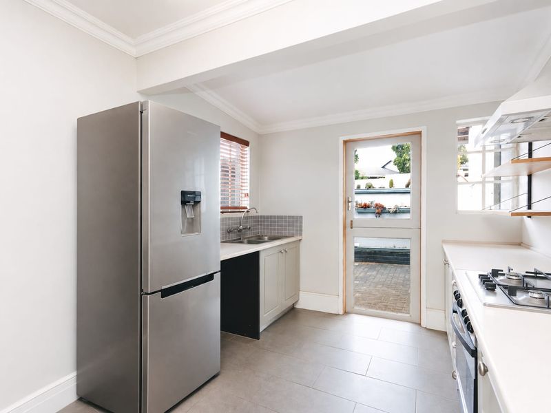 A clean, modern kitchen featuring built-in cabinetry, a gas cooktop with extractor, stainless steel sink, and direct access to the rear patio via a stable door.