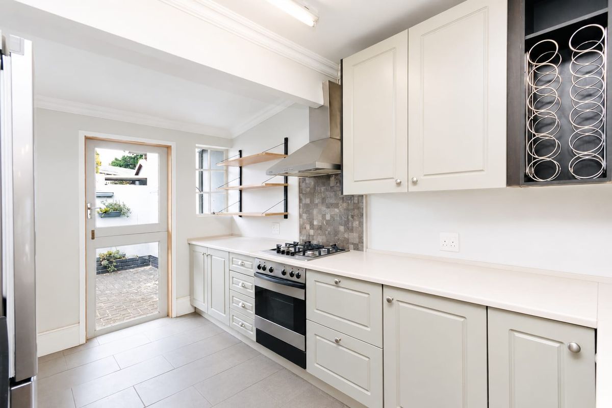 Modern kitchen featuring light-toned cabinetry, stone countertops, gas hob, stainless steel extractor, and direct access to a paved outdoor area.