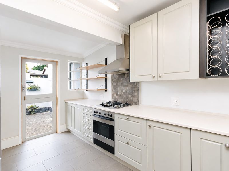 Modern kitchen featuring light-toned cabinetry, stone countertops, gas hob, stainless steel extractor, and direct access to a paved outdoor area.