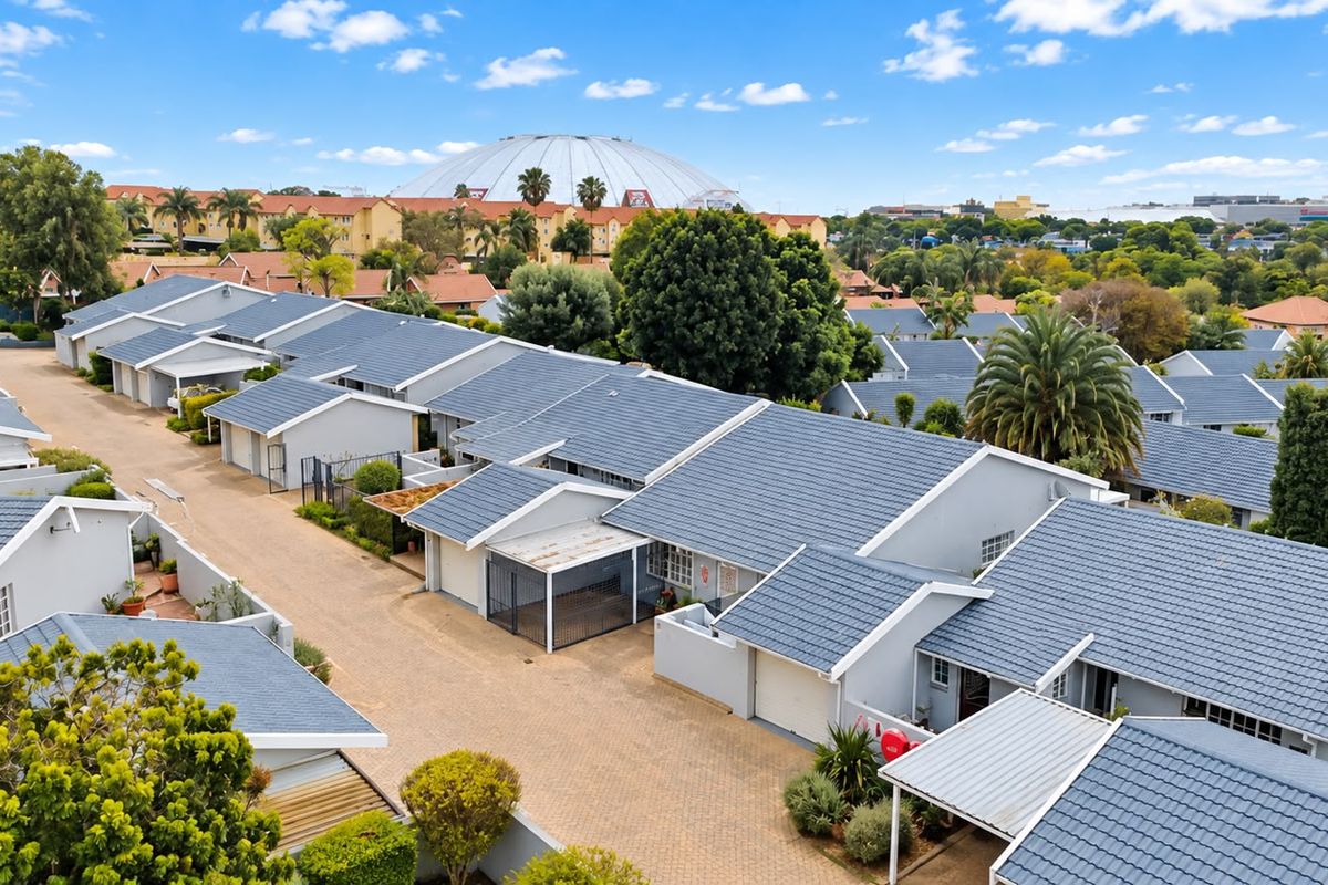 An aerial view of a residential townhouse complex featuring uniform tiled roofs, paved driveways, and integrated carports within a landscaped estate setting.