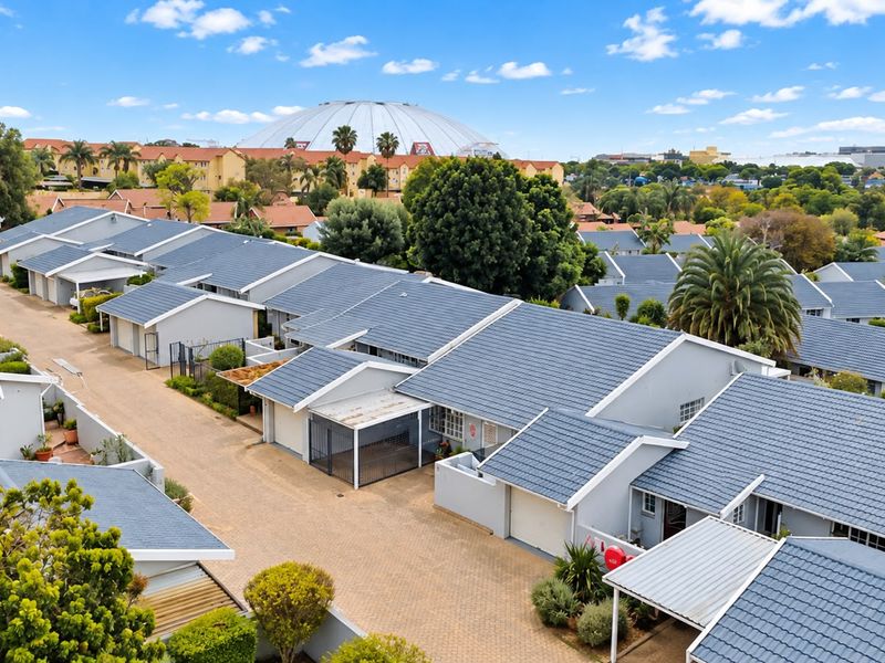 An aerial view of a residential townhouse complex featuring uniform tiled roofs, paved driveways, and integrated carports within a landscaped estate setting.