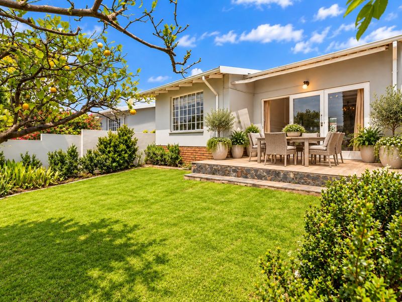 A well-maintained rear exterior featuring a raised stone-clad patio, sliding glass doors, and a lush, landscaped garden area.