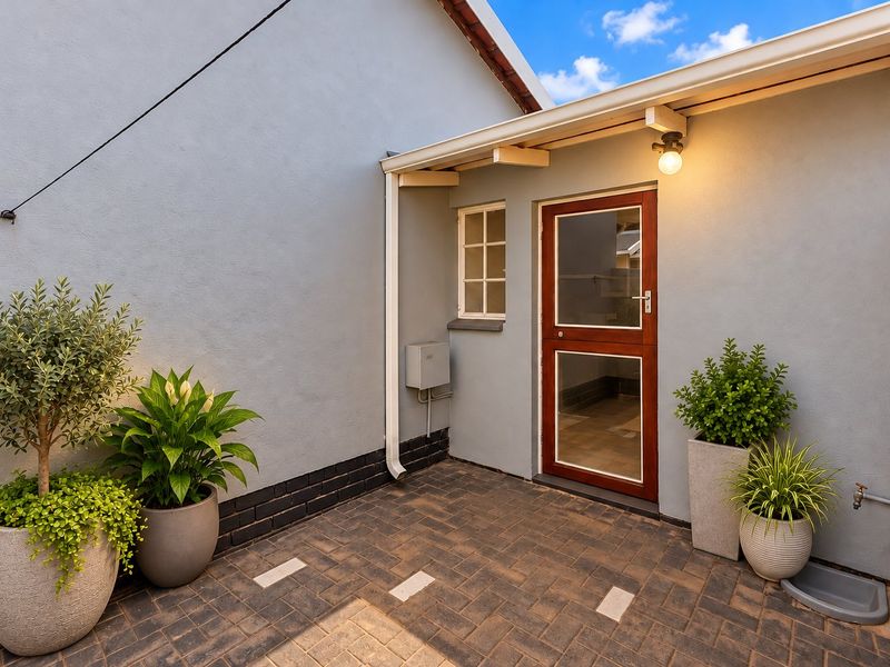 A well-maintained paved rear courtyard area featuring a secure external door, guttering, and an outdoor water tap.