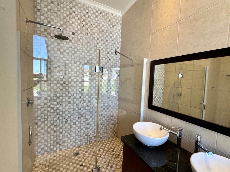 Modern bathroom featuring a walk-in shower with mosaic tiling, dual vessel sinks on a granite vanity, and a large wall-mounted mirror.