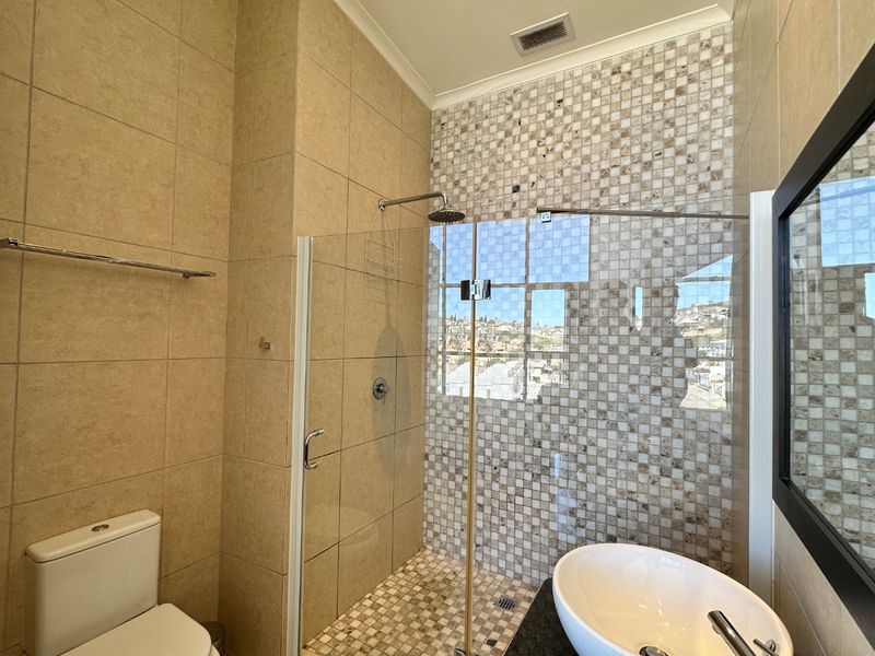Modern bathroom featuring a walk-in shower with glass screen, mosaic tile accents, vessel sink, and neutral ceramic wall and floor tiling.