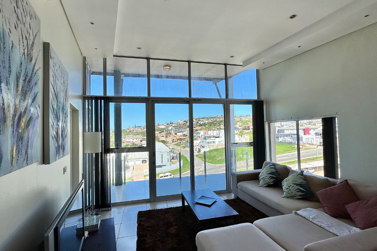 Bright living room featuring floor-to-ceiling windows, sliding glass doors, tiled flooring, and recessed lighting, offering expansive views of the surrounding neighborhood.