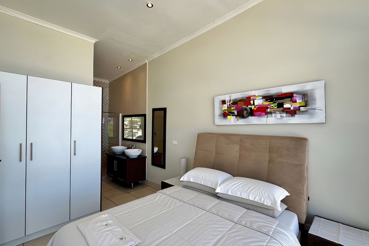 A well-maintained bedroom featuring a built-in wardrobe, recessed lighting, and an open-plan en-suite bathroom with a double vanity.
