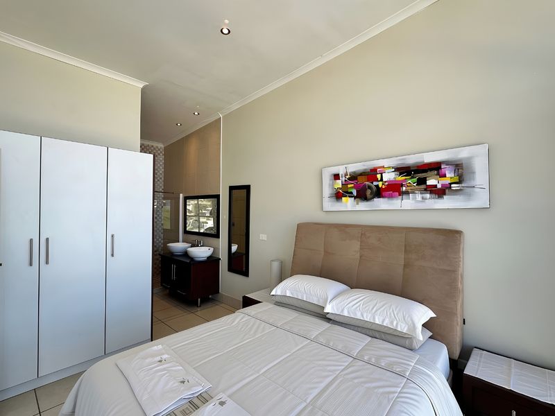A well-maintained bedroom featuring a built-in wardrobe, recessed lighting, and an open-plan en-suite bathroom with a double vanity.