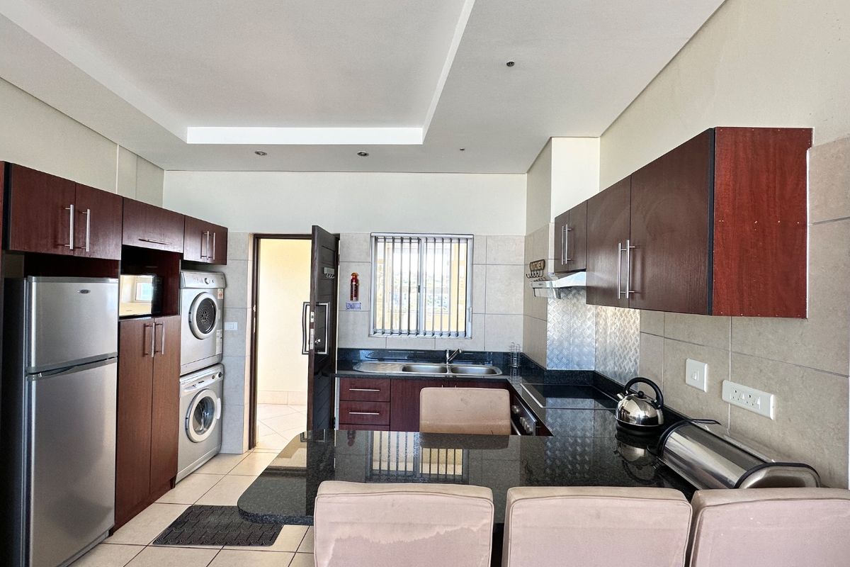 A well-maintained kitchen featuring dark wood cabinetry, granite countertops, a double basin sink, and integrated laundry appliances.