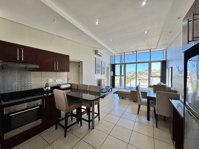 Open-plan living area featuring a modern kitchen with granite countertops, tiled floors, and floor-to-ceiling glass doors offering expansive views.