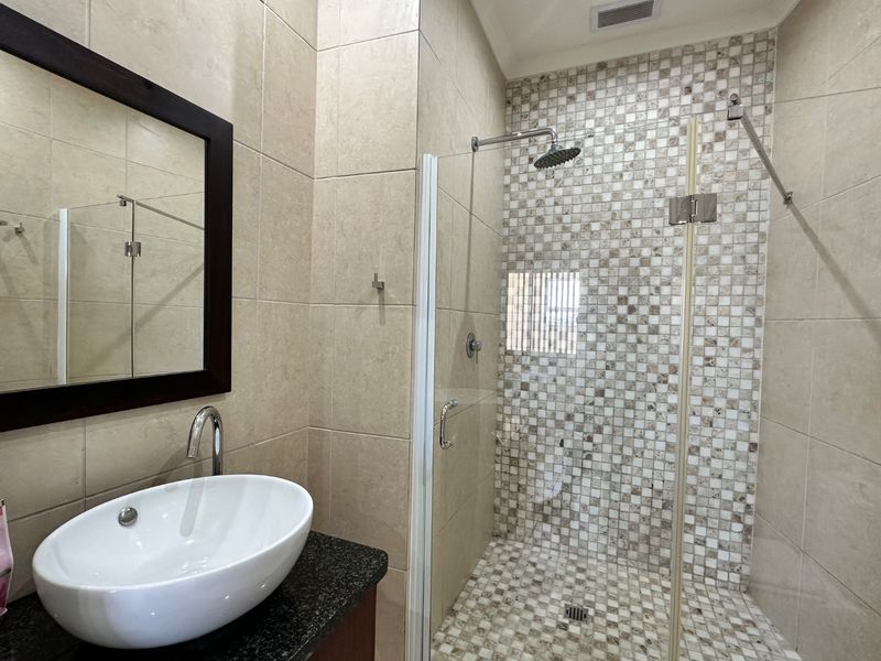 Modern bathroom featuring a vessel sink on a granite vanity, and a spacious walk-in shower with mosaic tile accents and a rain shower head.
